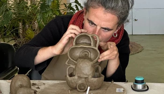 Woman carefully handbuilding clay sculpture at slow living pottery retreat in India.