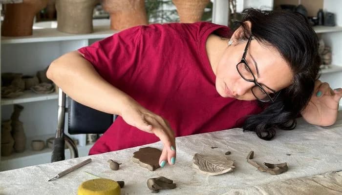 Woman shaping clay at a pottery retreat in India surrounded by mountain greenery.