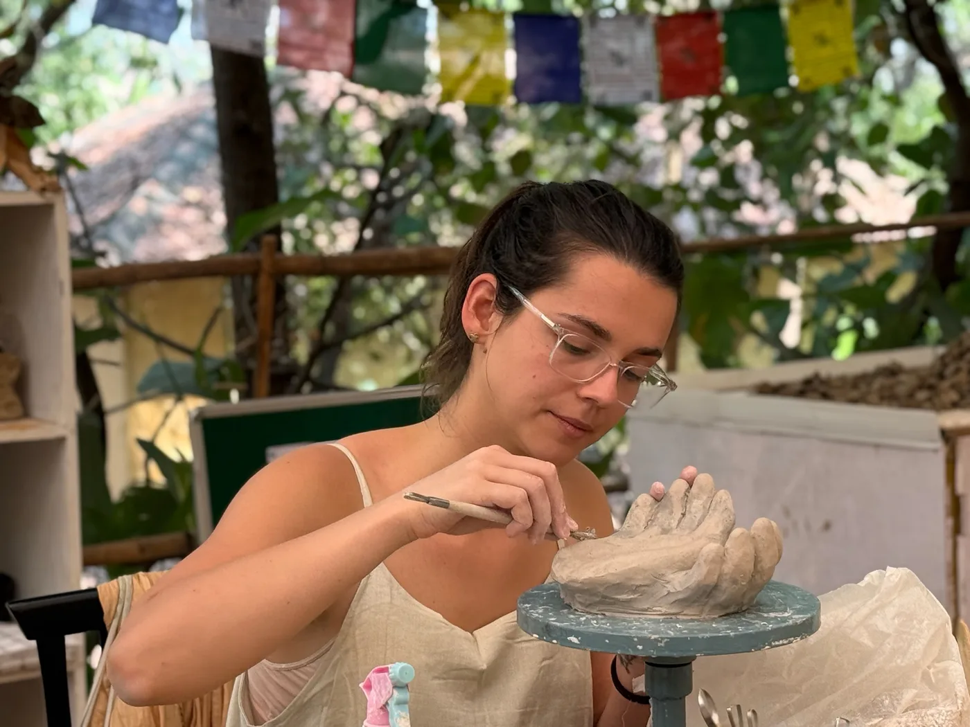 A retreat participant sculpting clay by hand in the open-air Dharamkot Studio Goa pottery space.