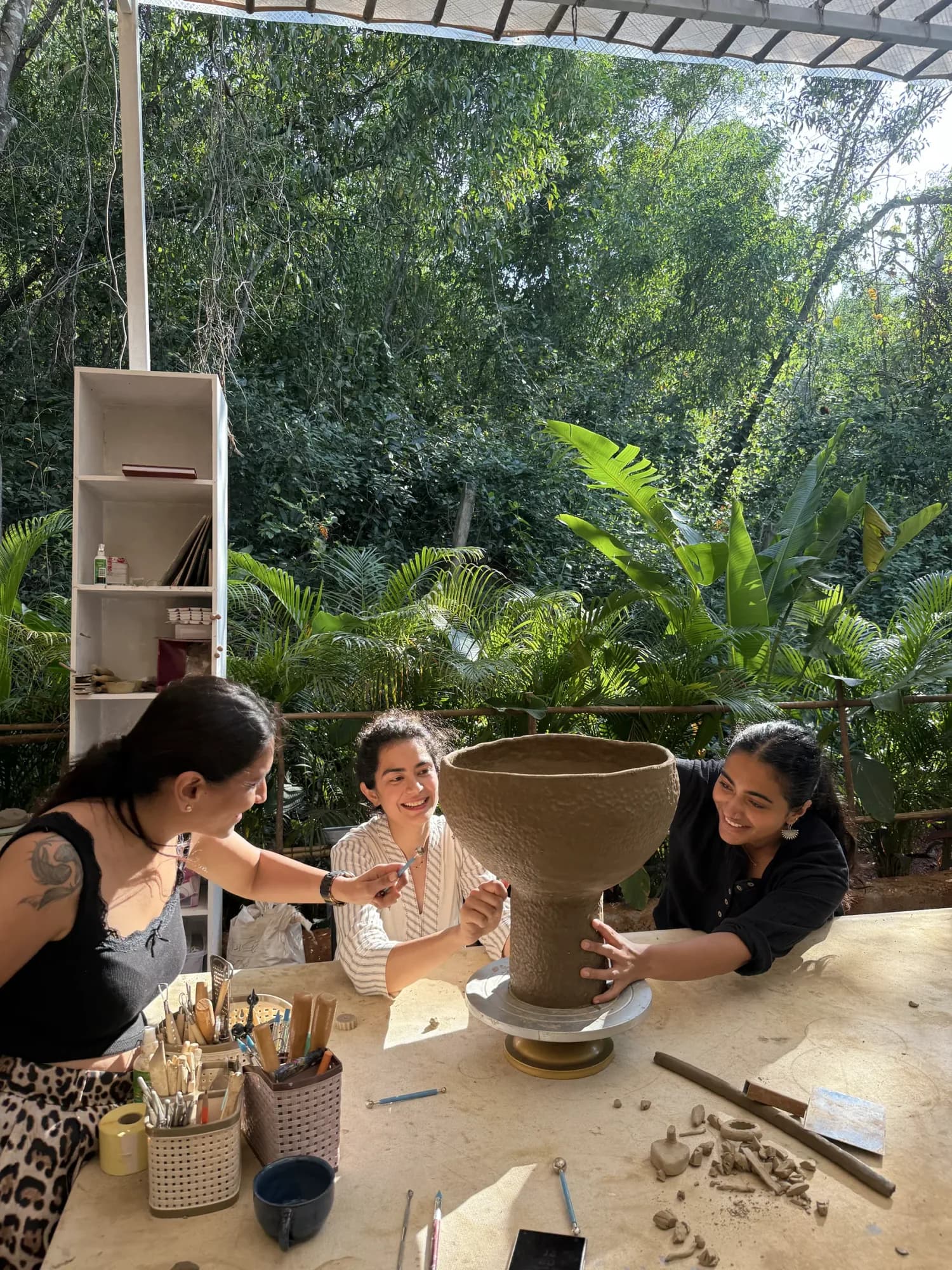 Students shaping clay beside lush cashew trees at Dharamkot Studio Goa in Mandrem.