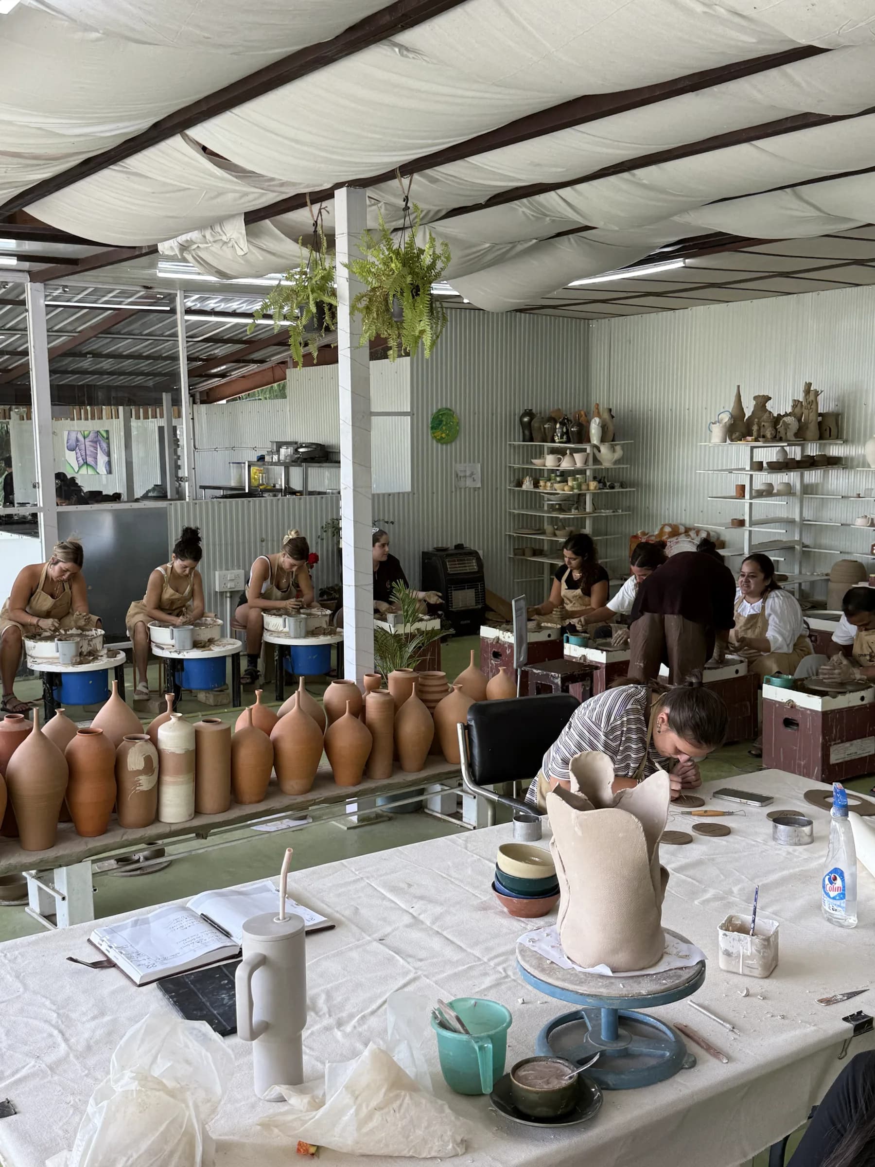 Students practicing pottery inside Dharamkot Studio in Himachal Pradesh with finished clay forms in the foreground.