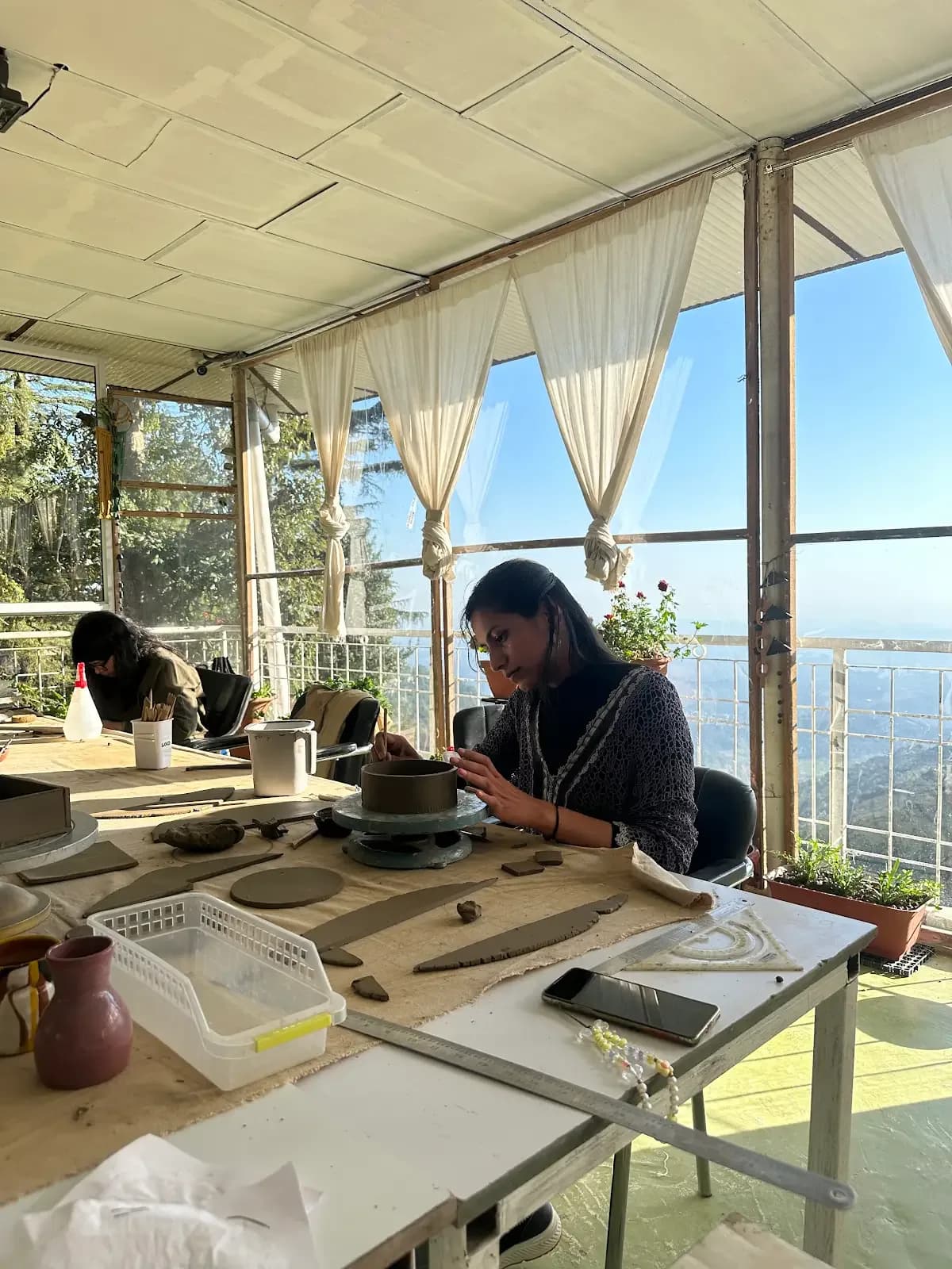 Pottery wheel practice beside large mountain-view studio windows in Dharamkot.
