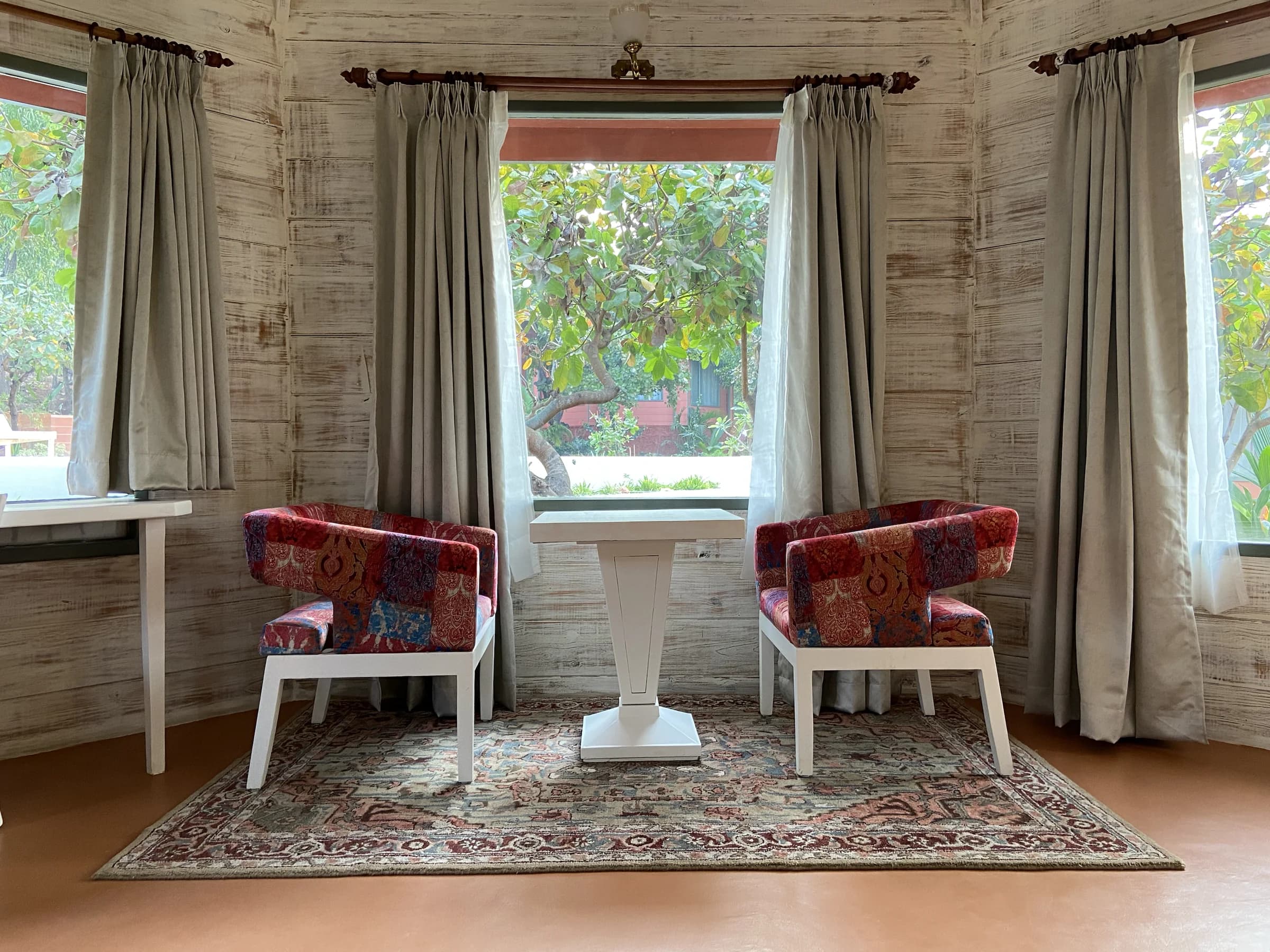 A quiet seating corner with patterned chairs beside wide cottage windows looking out to the garden.