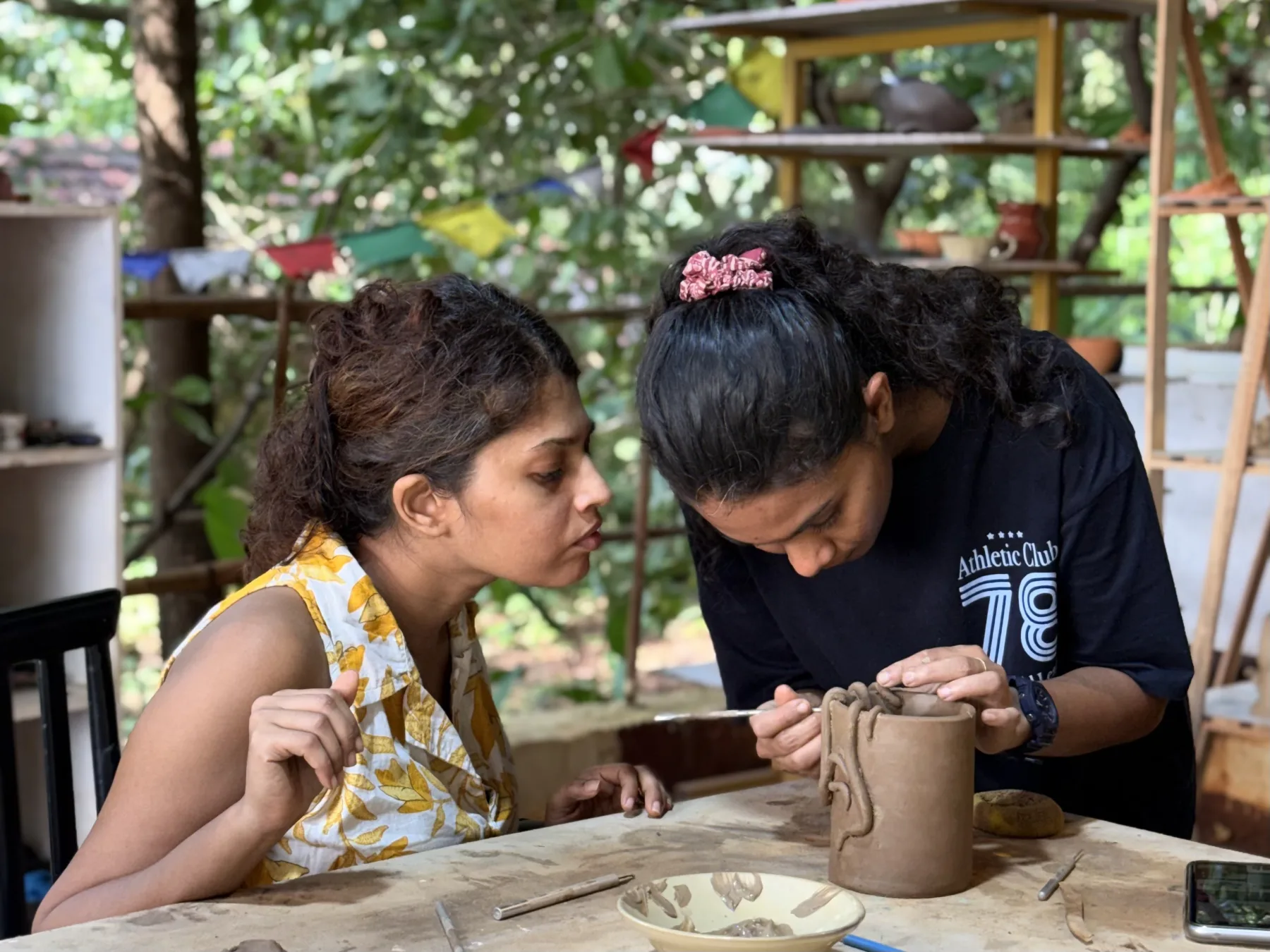 A facilitator guiding a participant as she decorates a hand-built clay vessel in the Goa studio.