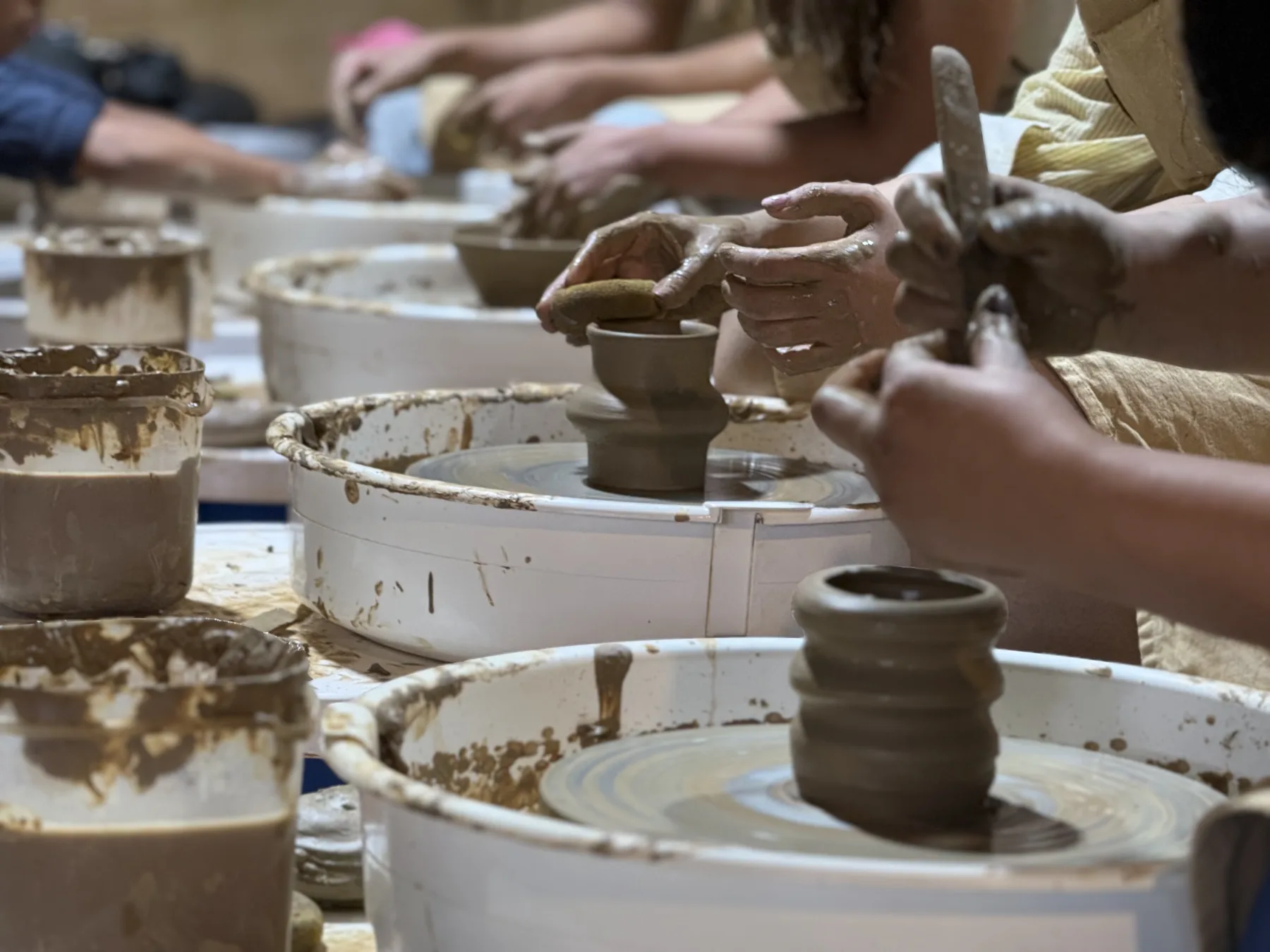 Clay-covered hands shaping small wheel-thrown pots during a beginner pottery session in Goa.