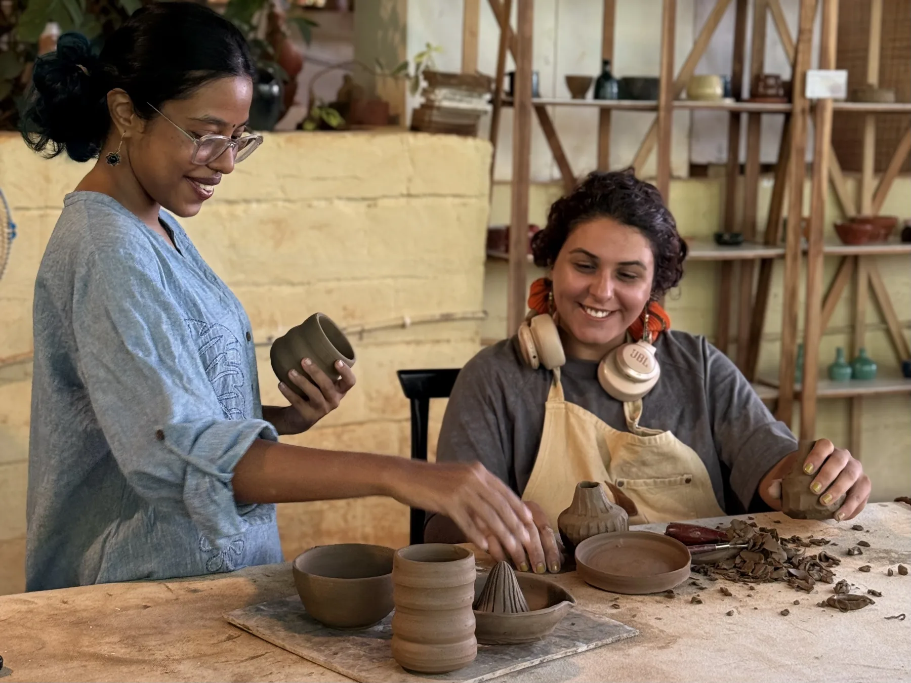 A Goa pottery instructor reviewing finished clay forms with a smiling retreat participant.