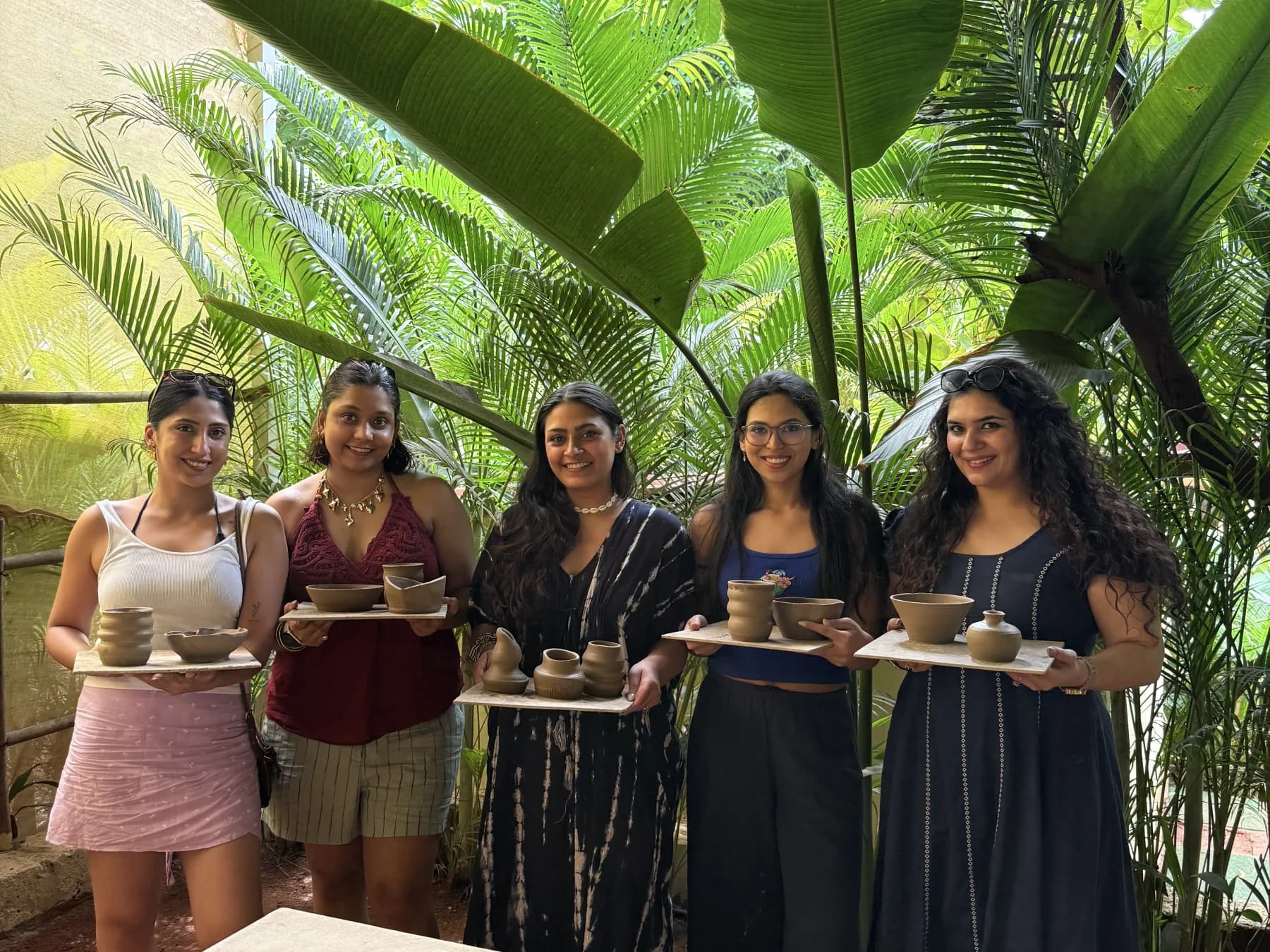 Five pottery retreat participants holding their finished wheel-thrown pieces in the tropical Goa studio.