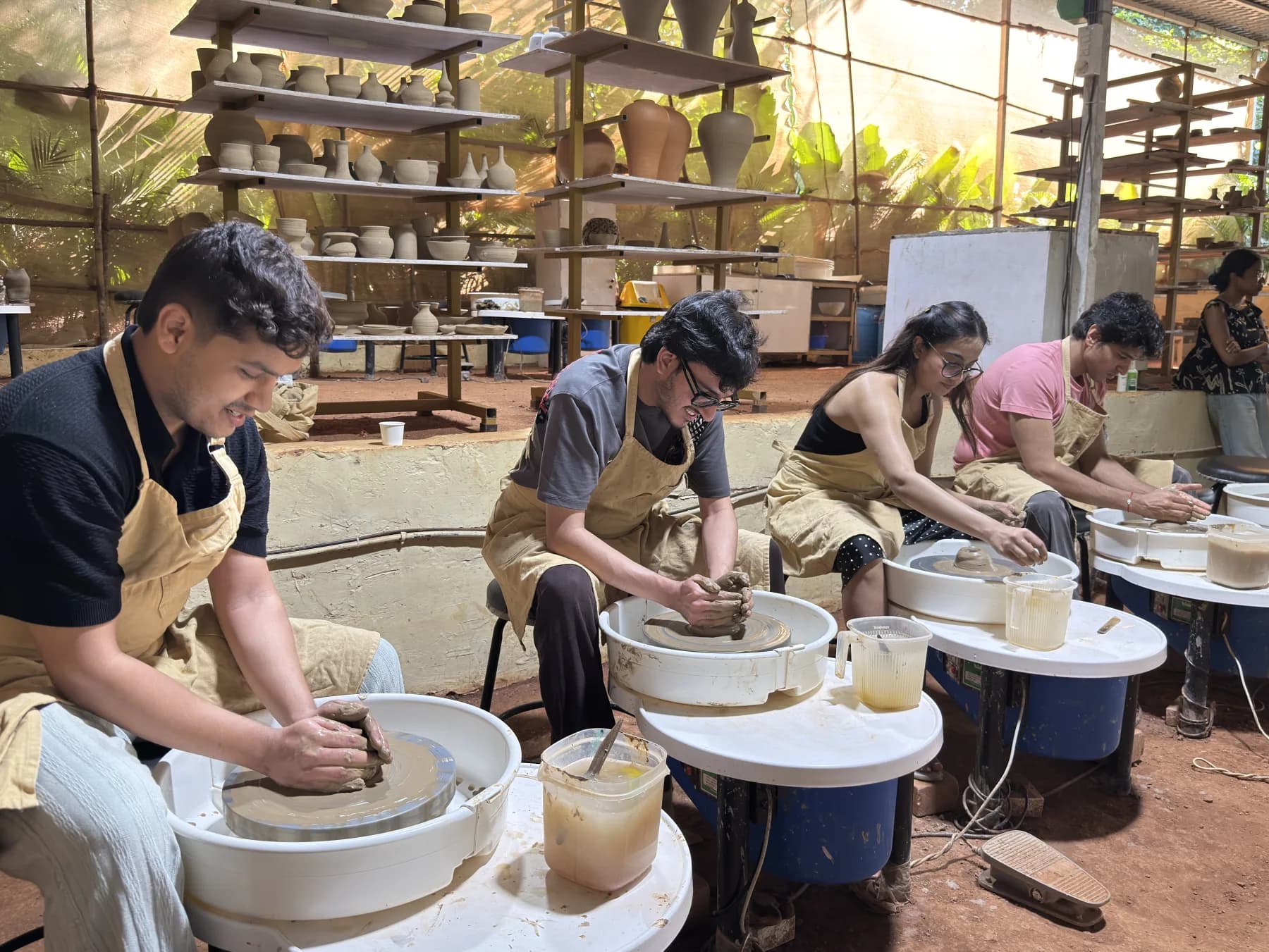 Four retreat participants learning wheel throwing side by side in the open-air pottery studio in Goa.