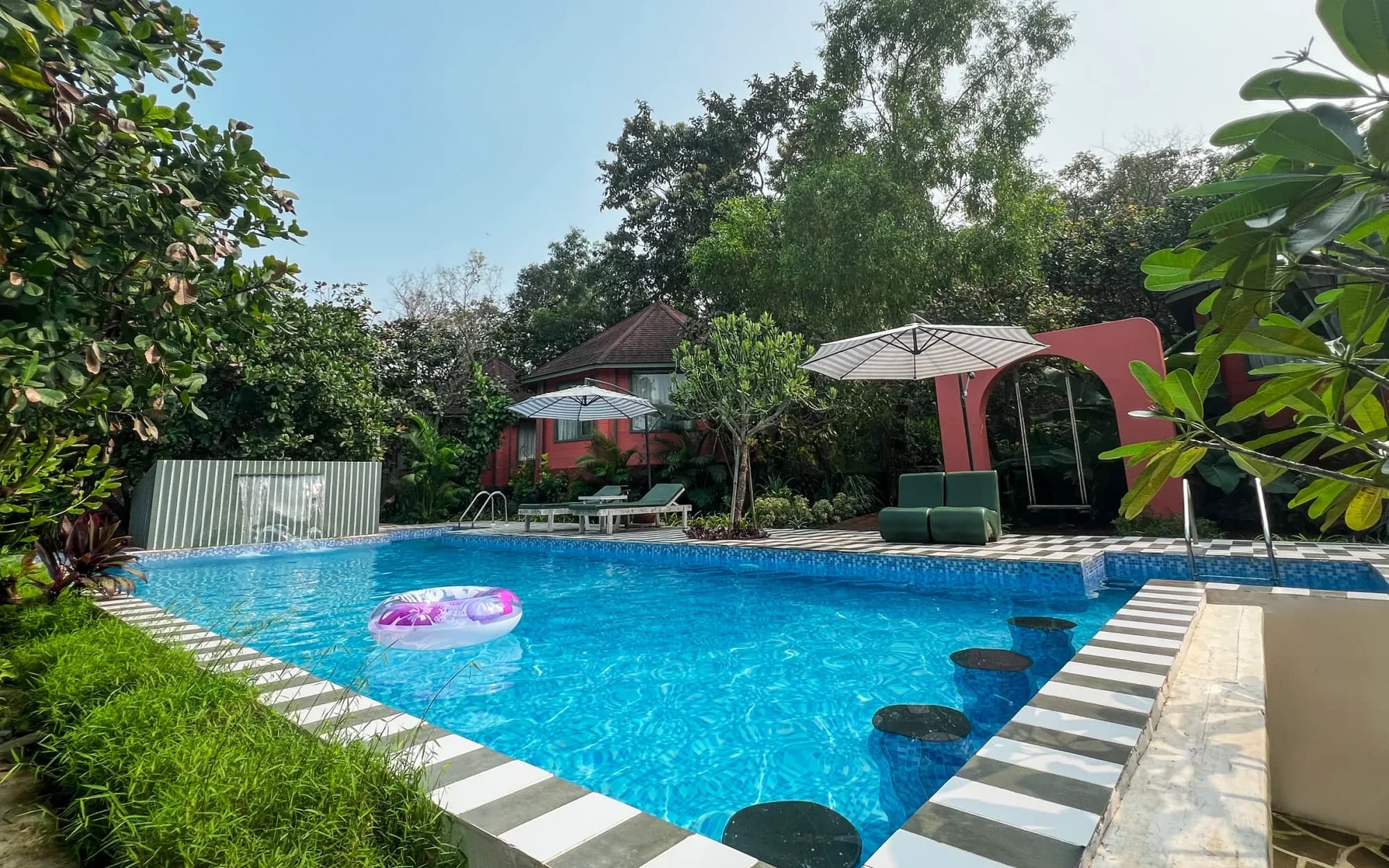 A quiet pool and tropical garden framed by tall palms and retreat cottages in Mandrem, Goa.