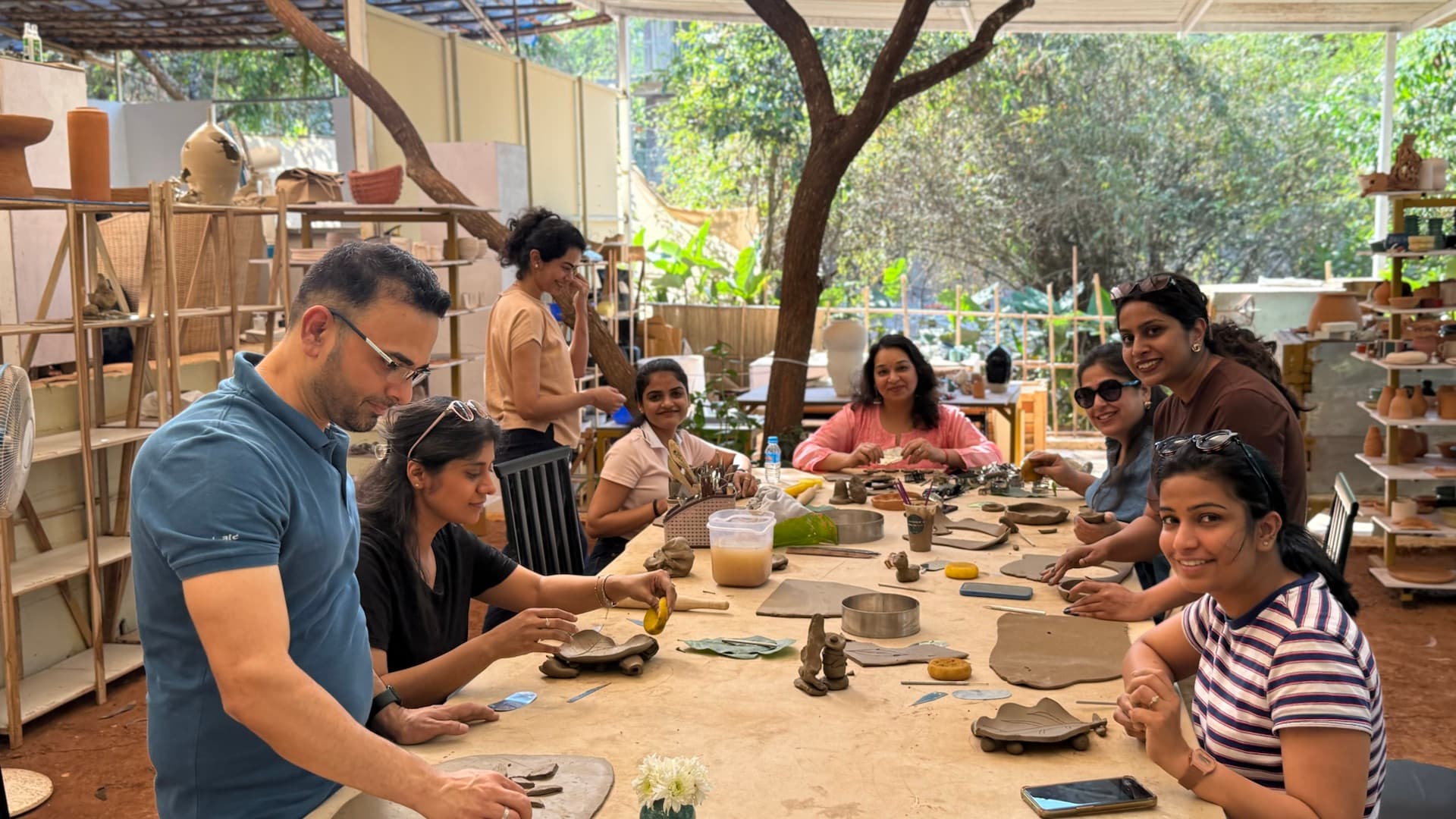 A group of pottery retreat participants hand building together around a long table in the open Goa studio.