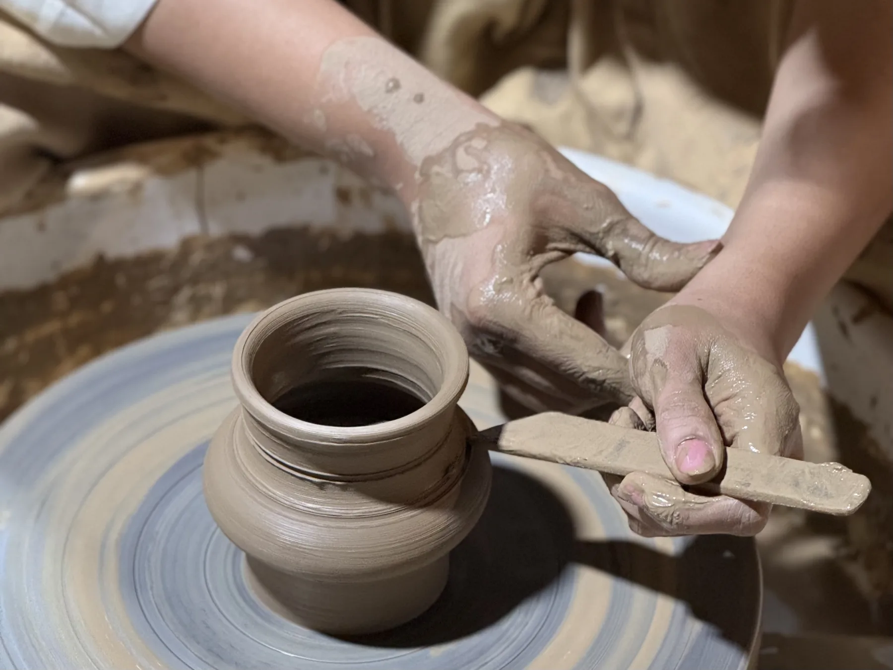 A pottery retreat participant trimming the foot of a wheel-thrown clay vessel in the Goa studio.