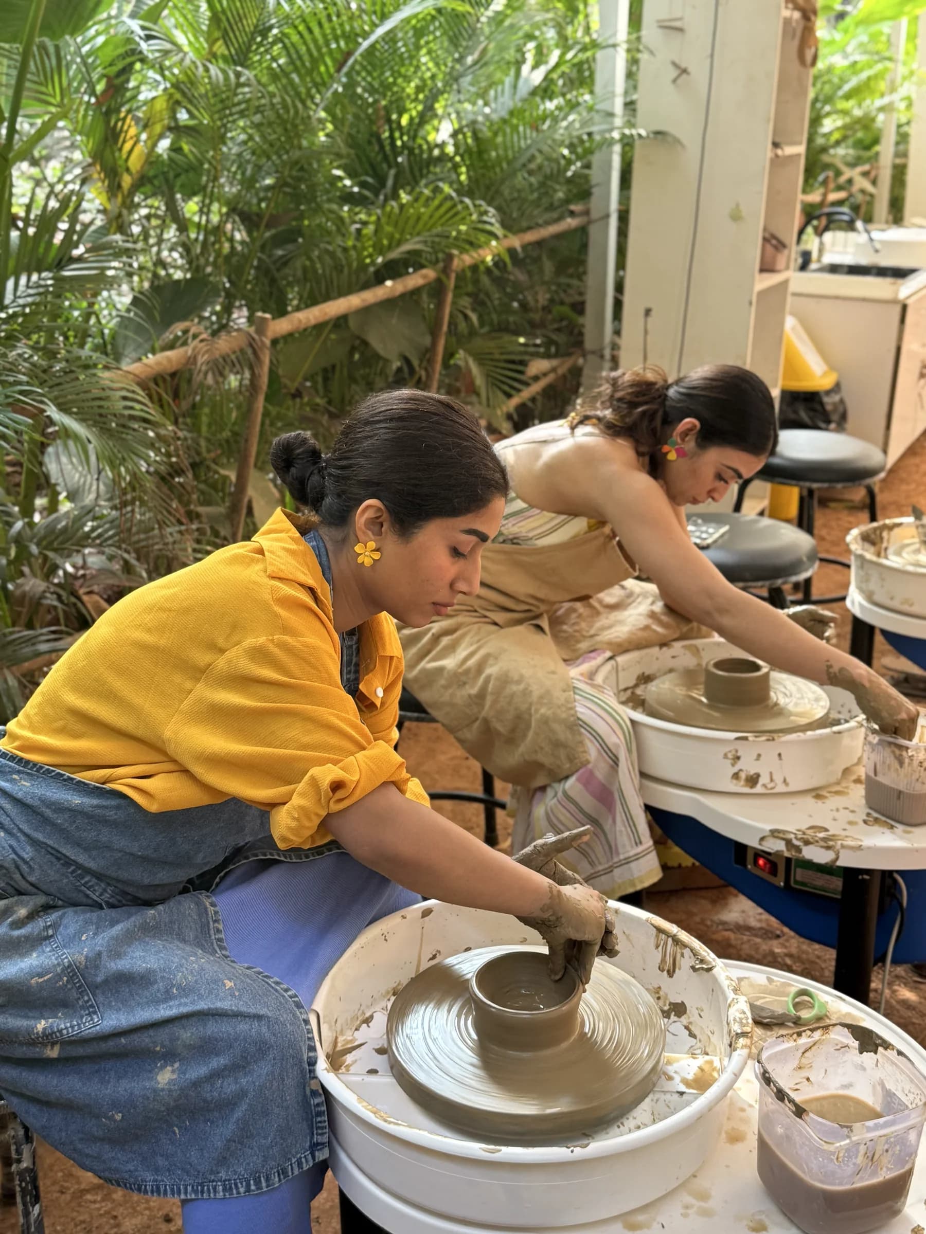 Two participants shaping clay at pottery wheels in Goa.