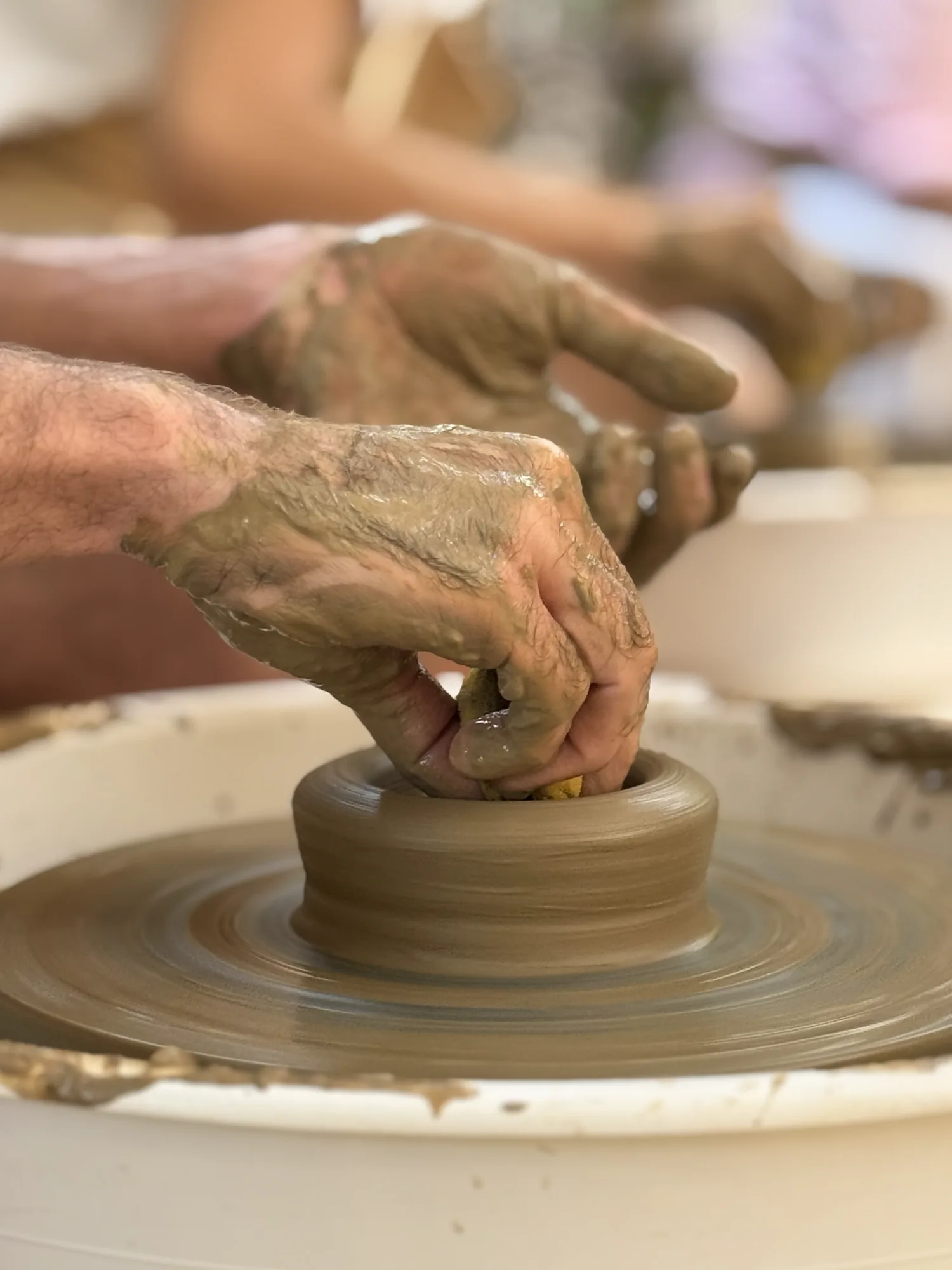 Close view of clay-covered hands learning wheel-throwing technique in Goa.
