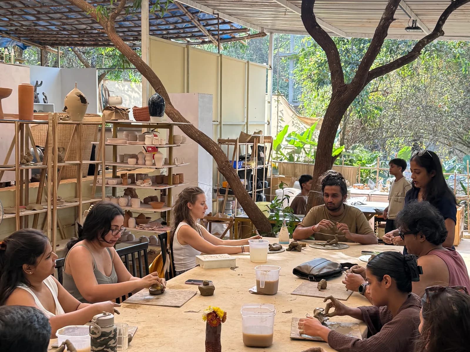 Participants shaping clay around a large shared table during a private group pottery workshop at Dharamkot Studio in Goa.