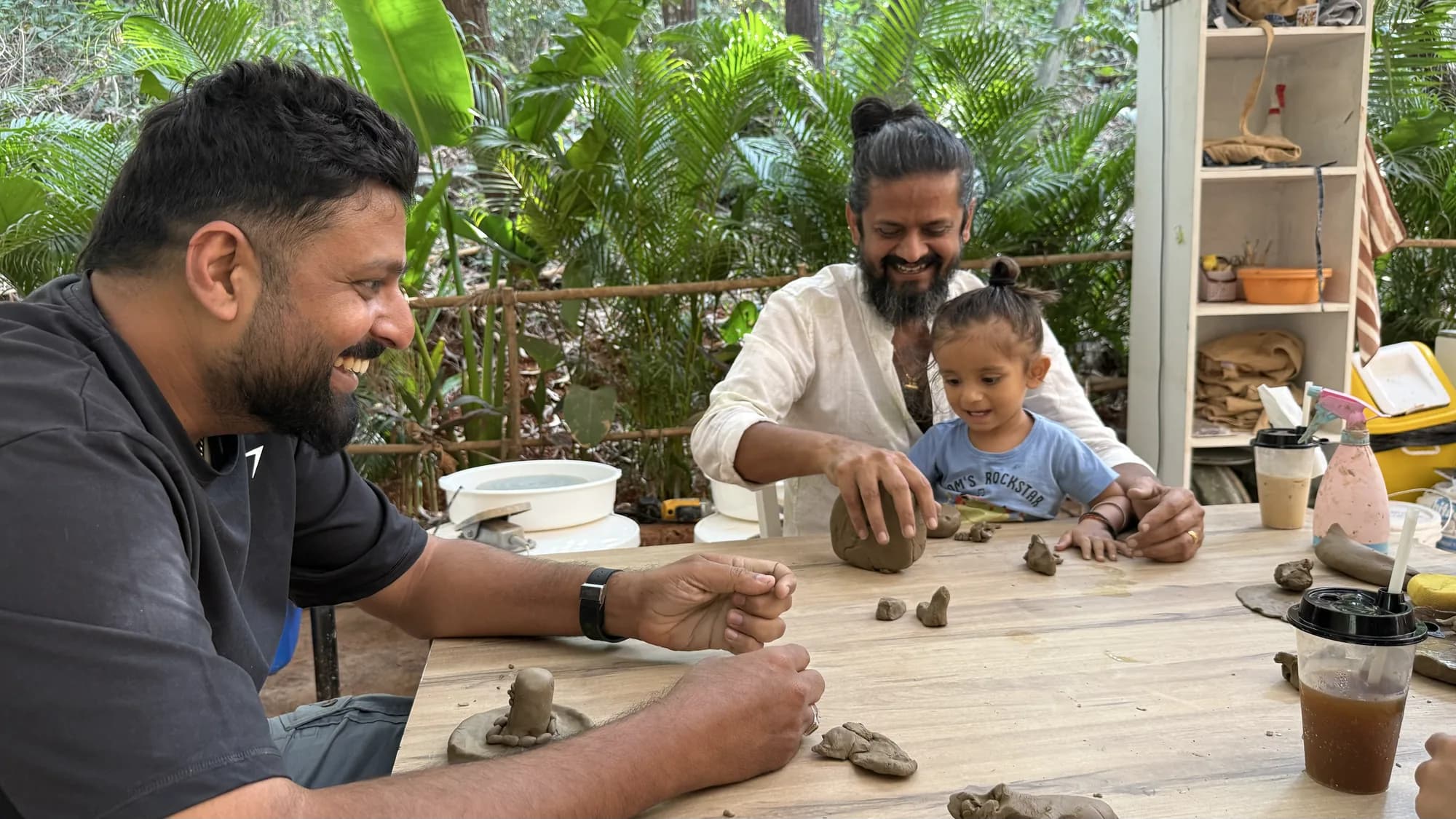 Adults and a young child smiling and playing with clay together during an open clay session in Goa.