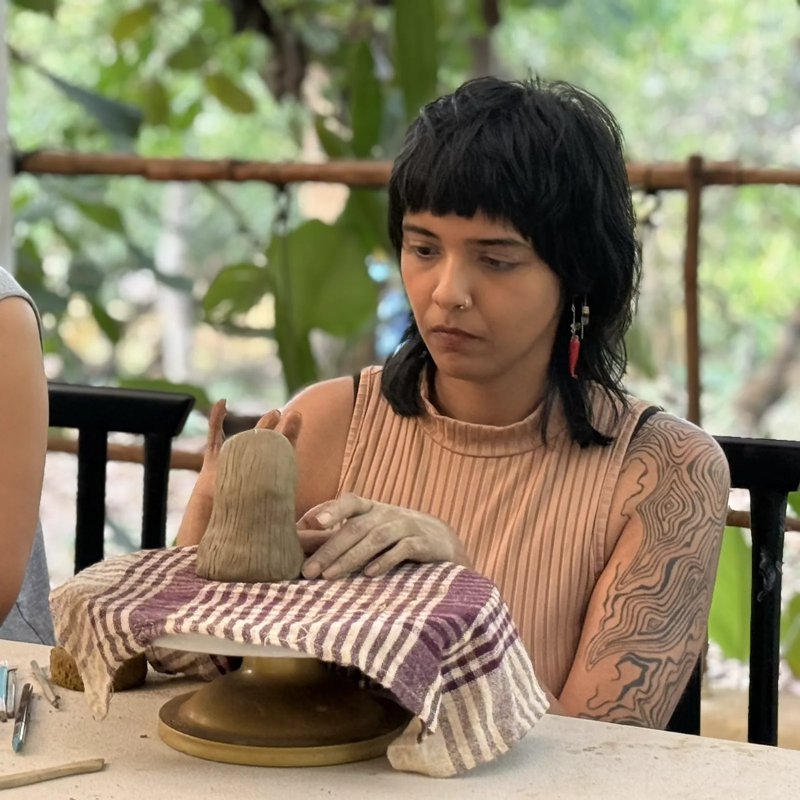 Participant shaping a small figurative clay sculpture on a banding wheel during the Goa Open Clay Session.
