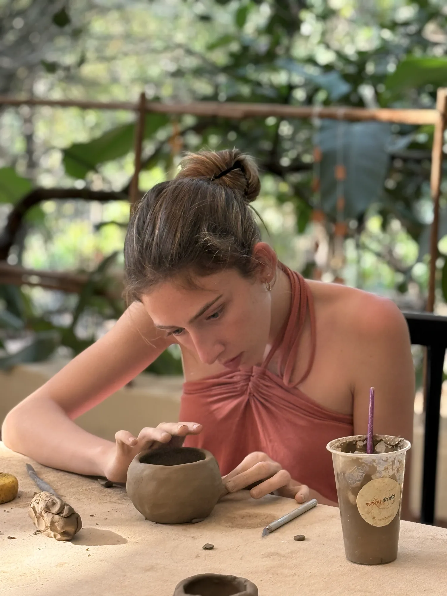 Participant refining the rim of a small hand-built clay vessel during the Goa Open Clay Session.