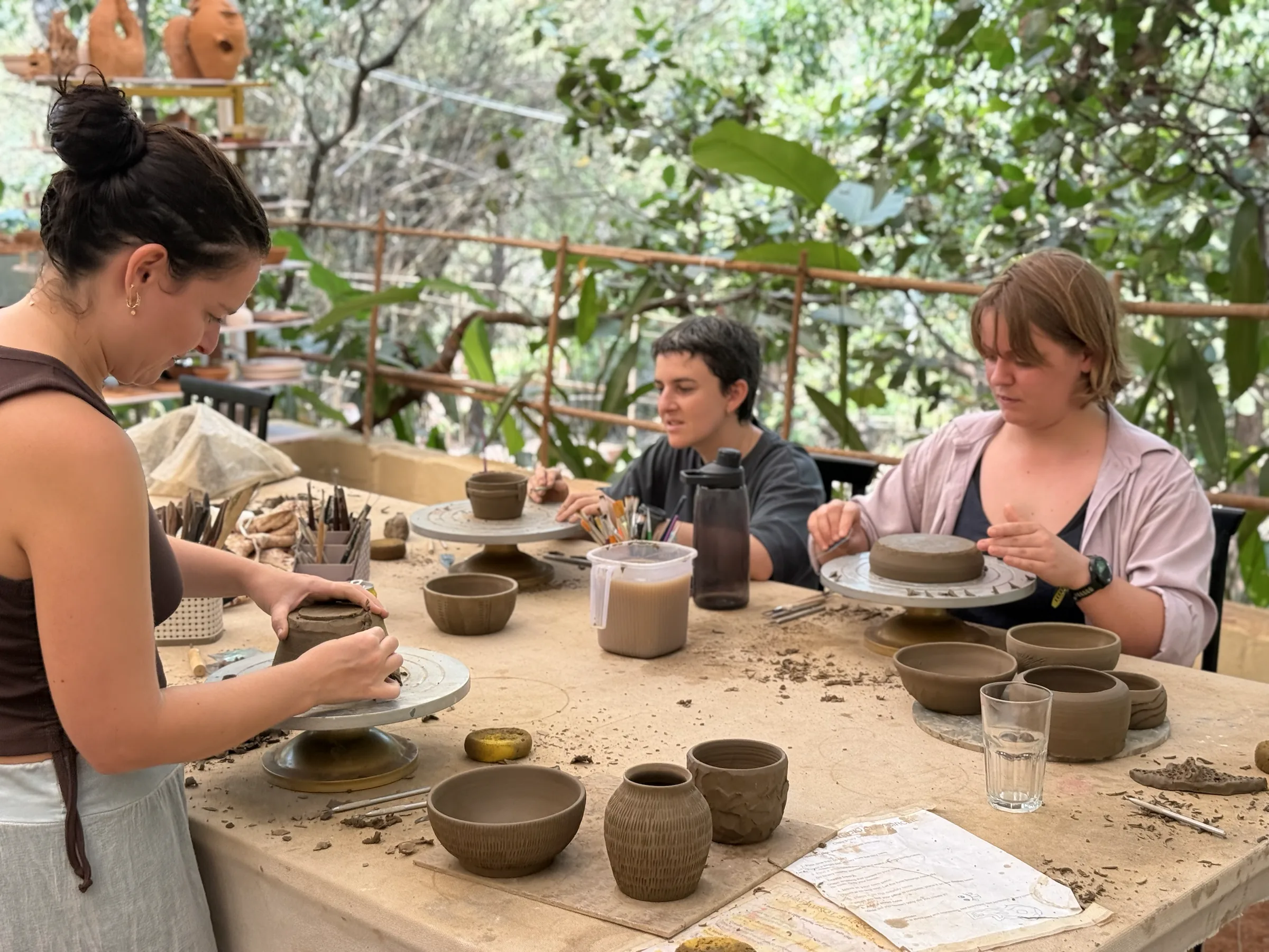 Three participants quietly refining bowls and vessels by hand during the Sculpt & Shape workshop in Goa.
