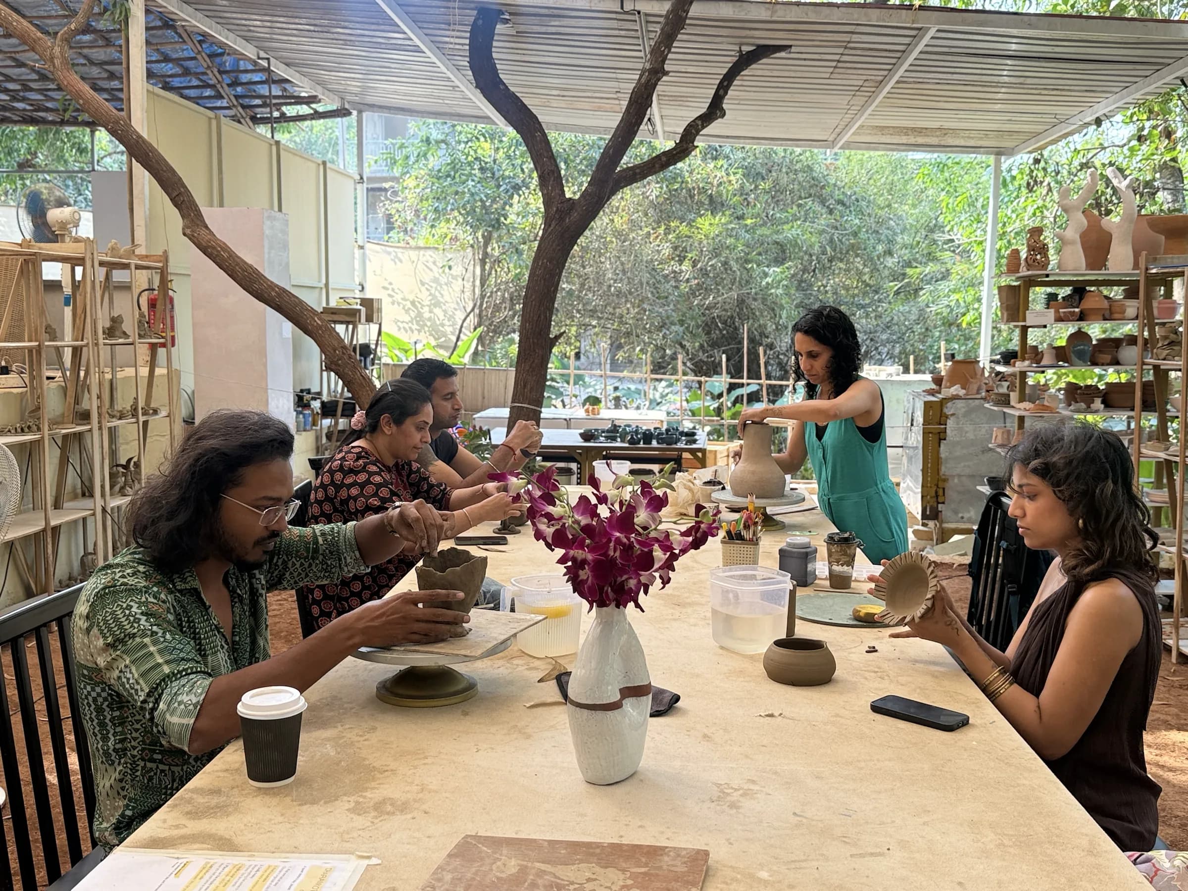 Participants handbuilding bowls and vases around a long table in Dharamkot Studio's open-air Goa workshop.