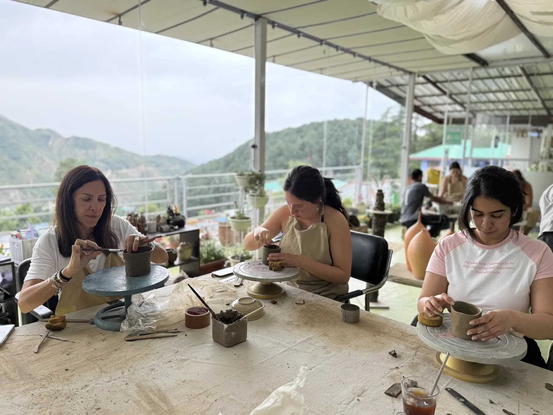 Participants shaping clay at a table with the Himachal mountain studio view behind them.