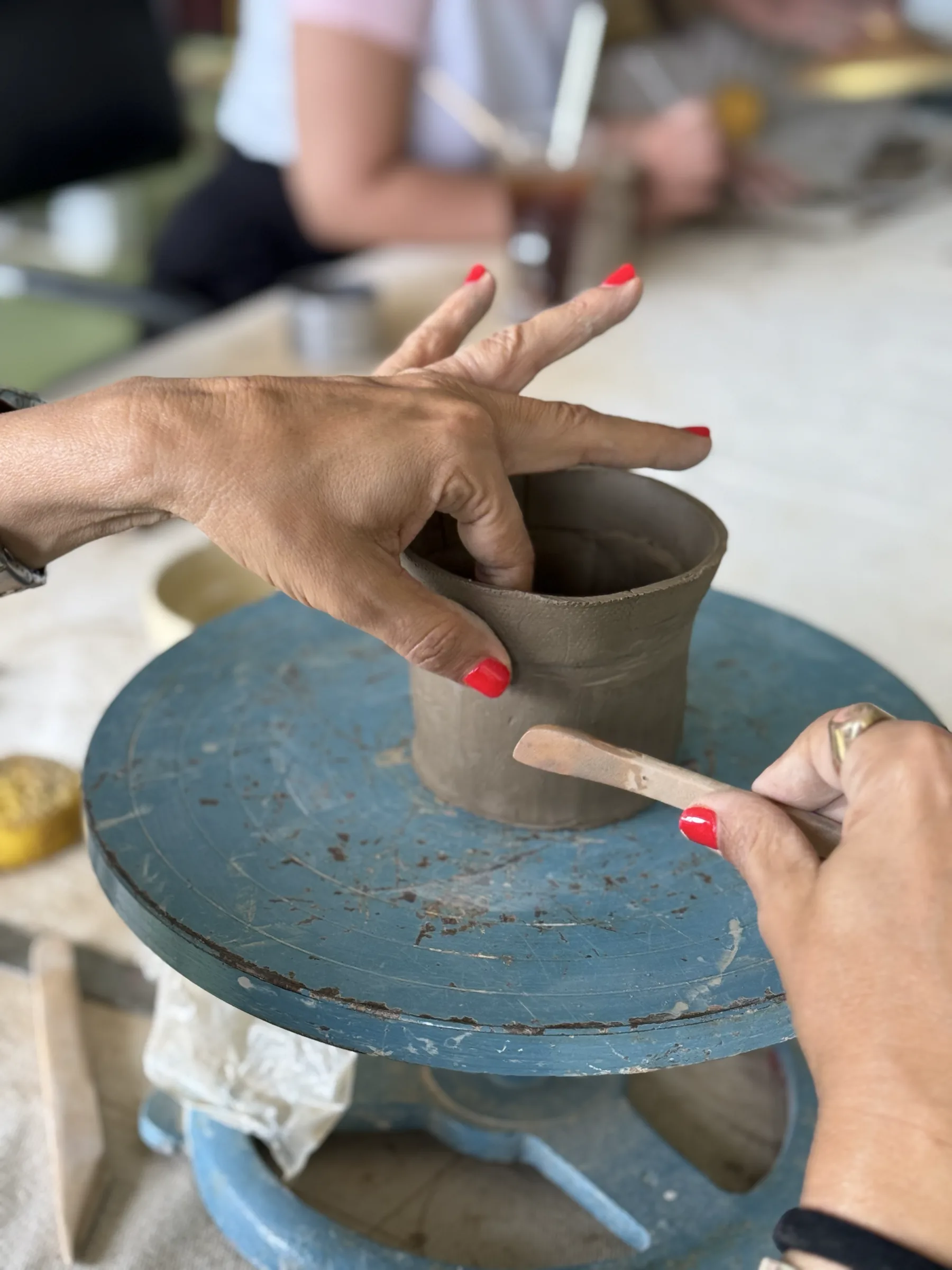 Hands shaping a clay vessel on a banding wheel during the Himachal Open Clay Session.