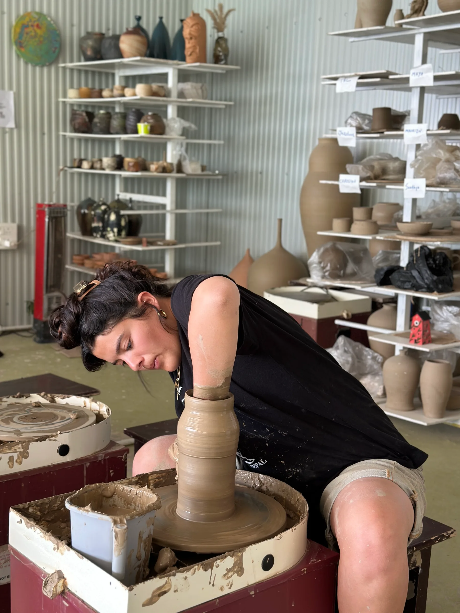 Student concentrating on a wheel-thrown vessel inside the Dharamkot Studio Himachal workshop space.