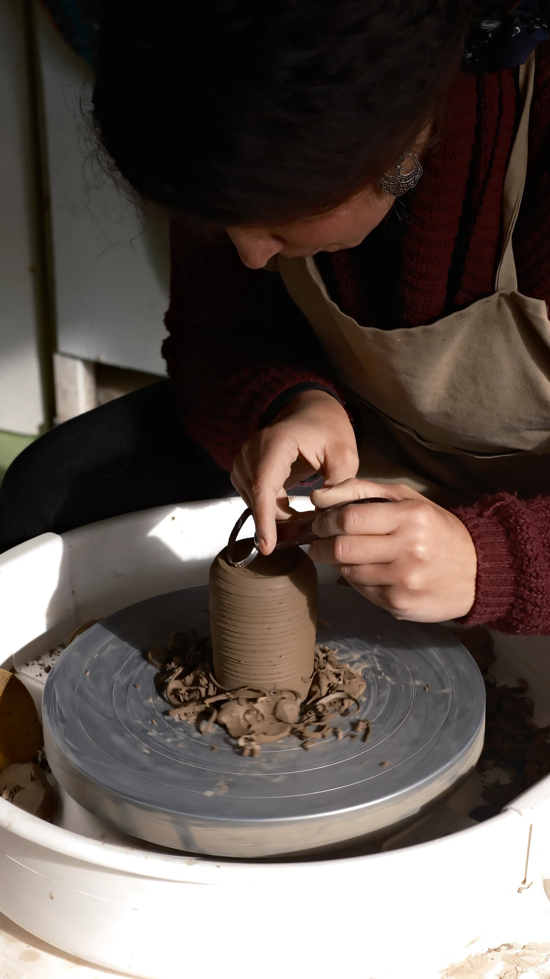 Student trimming and refining a wheel-thrown form during the Art of Wheel Throwing course.