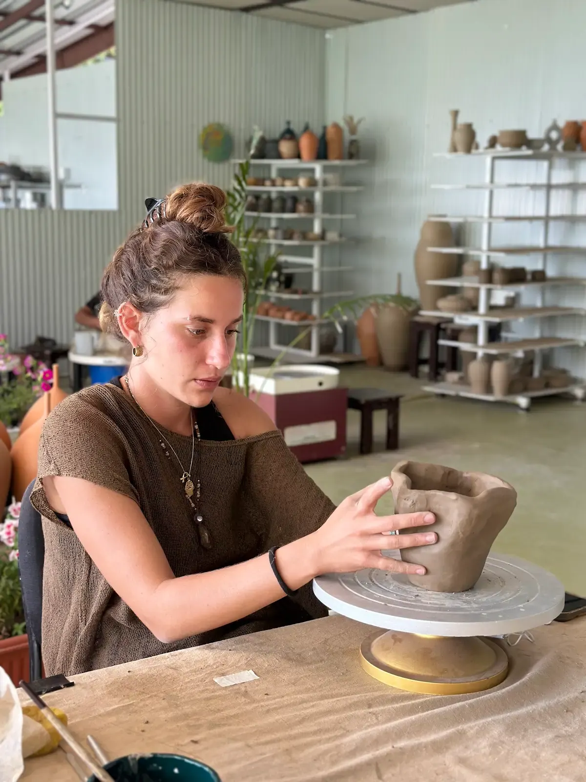 Participant shaping a large hand-built ceramic vessel on a banding wheel at Dharamkot Studio.