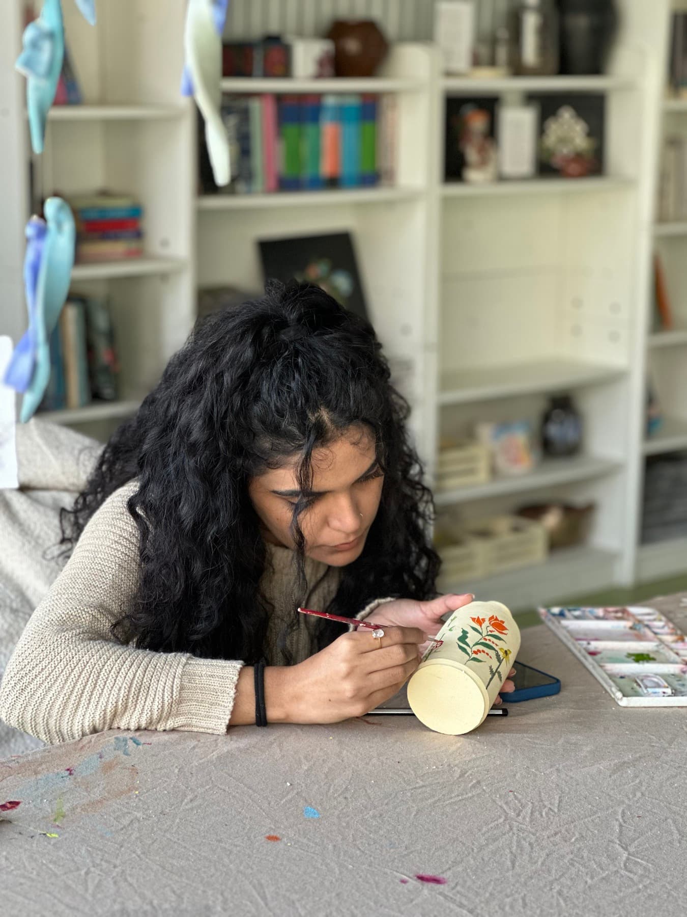 Participant painting orange flowers and green leaves on a cream ceramic vase during the Paint on Pottery workshop at Dharamkot Studio in Himachal Pradesh.