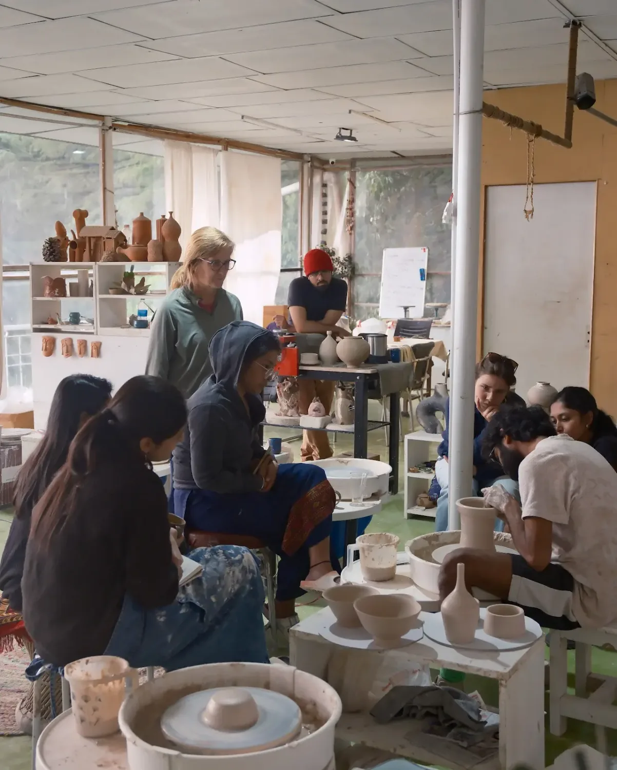 Instructor guiding pottery school students during wheel throwing practice at Dharamkot Studio.